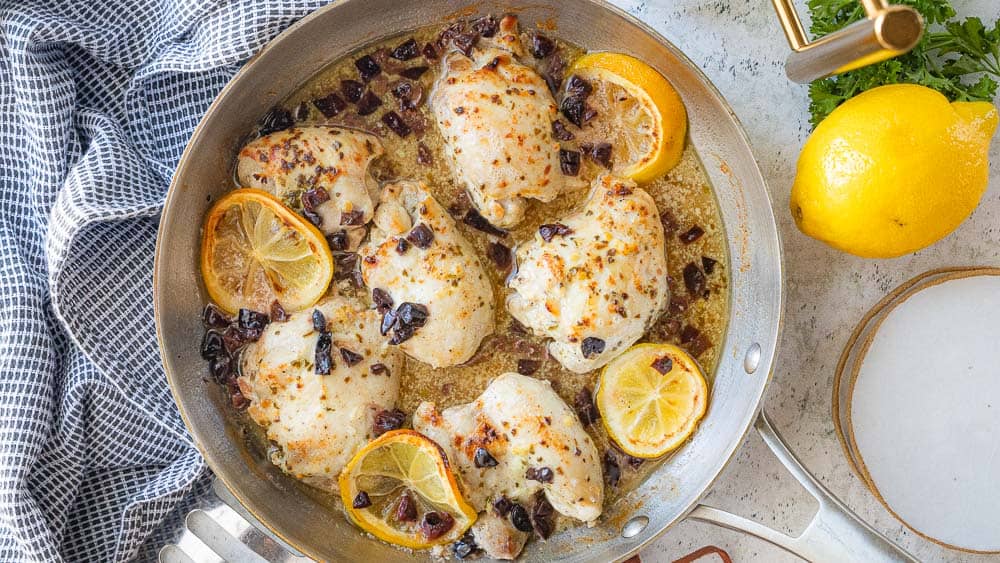 chicken thighs in skillet with lemon slices and olives