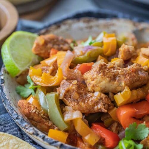 sliced and sauteed peppers in bowl with seasoned chicken