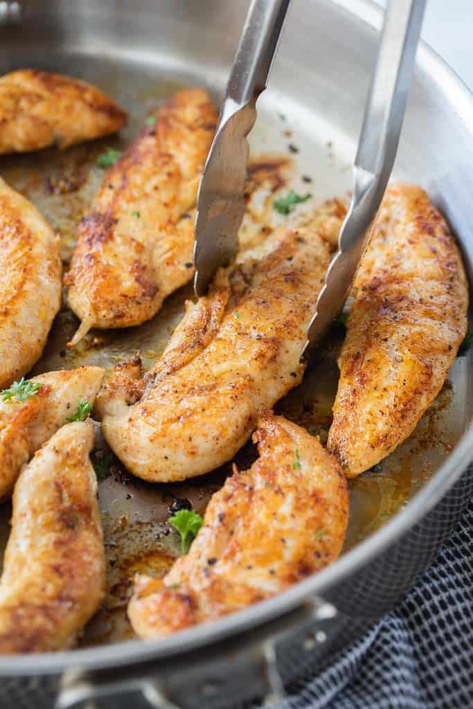 tongs picking up chicken tender in pan