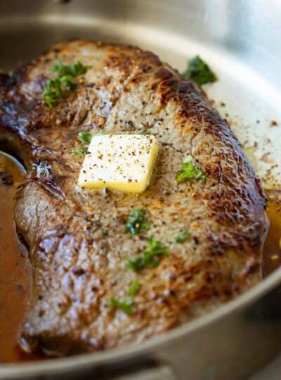 close up of seasoned sirloin steak in pan topped with melting butter