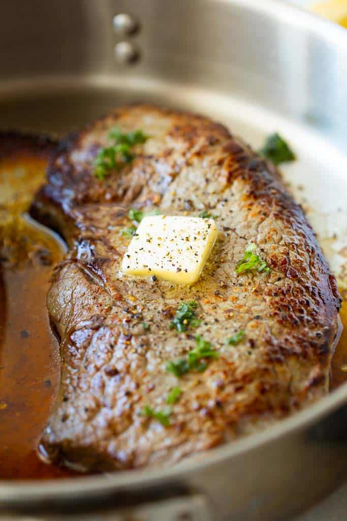 seasoned sirloin steak in pan topped with melting butter