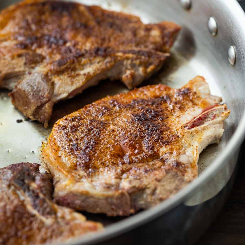 Close up of thin pork chops in a skillet.