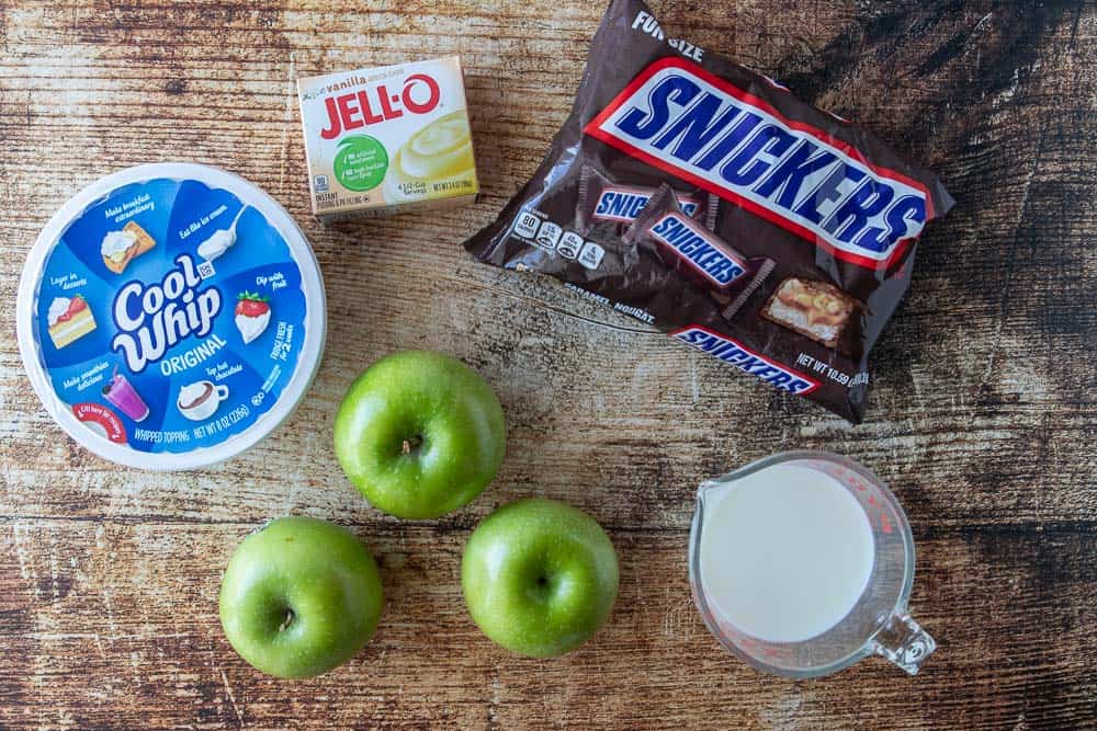 cool whip, vanilla pudding, snickers bars, green apples and milk displayed