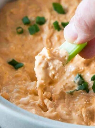 a hand scooping chicken buffalo dip with a celery stick