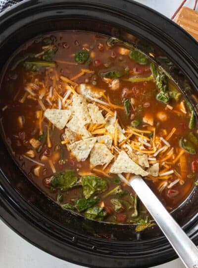 crockpot chicken tortilla soup topped with shredded cheese and crushed chips