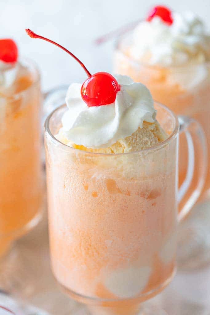 orange ice cream float topped with maraschino cherry and whipped topping