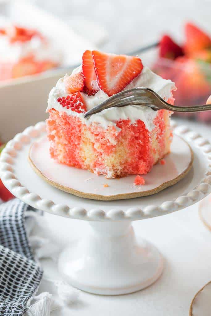 fork slicing into piece of strawberry cake on plate