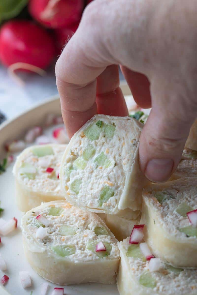 hand picking up a tortilla roll-up from plate