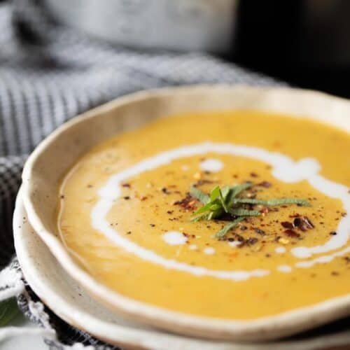 creamy squash soup in bowl garnished with coconut milk swirl and red pepper flakes