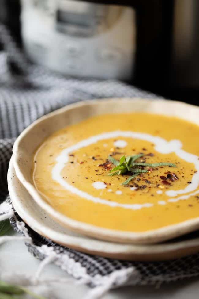 creamy squash soup in bowl garnished with coconut milk swirl and red pepper flakes