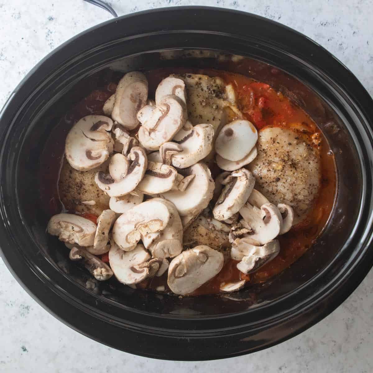 sliced mushrooms added to slow cooker with chicken thighs