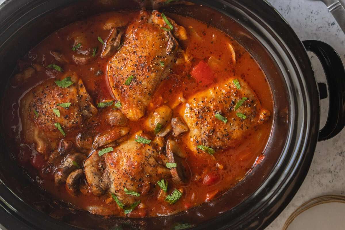 top down view of chicken thighs submerged in tomato and mushroom sauce