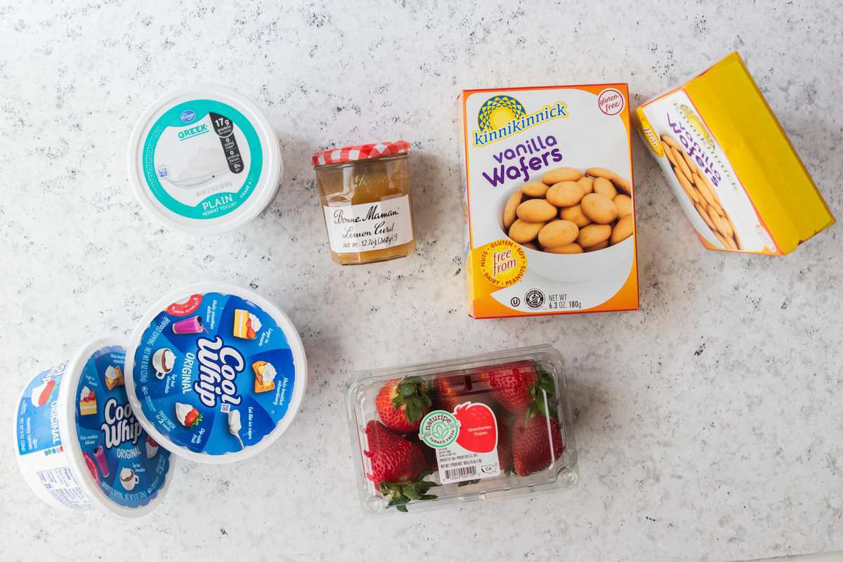 Greek yogurt, lemon curd, vanilla wafers, strawberries and cool whip displayed on a counter