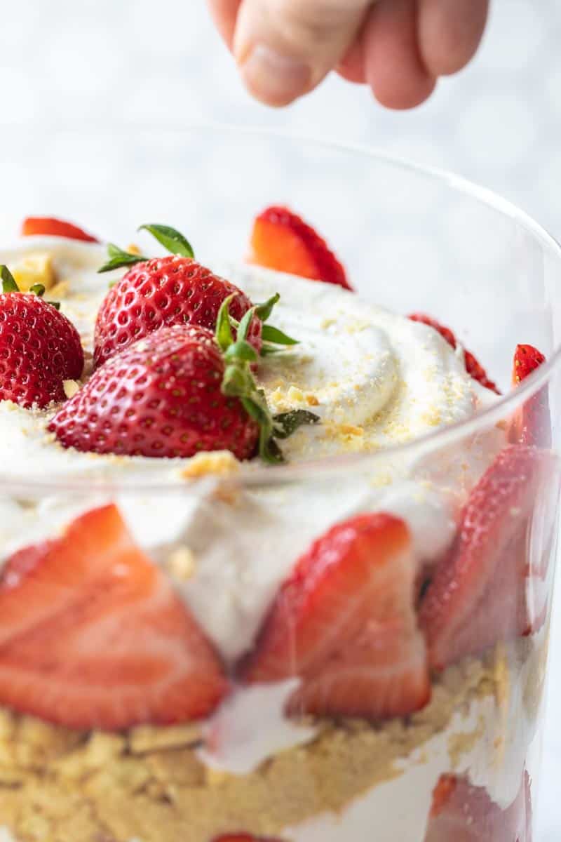 hand sprinkling topping on berry trifle dessert