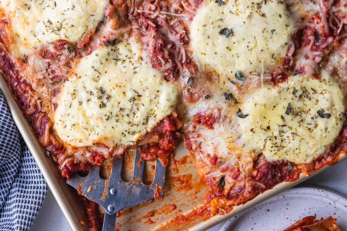 spatula scooping slice of lasagna from sheet pan