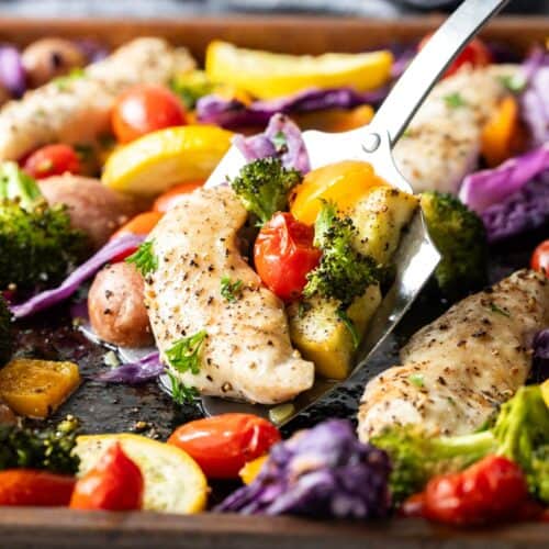 spatula scooping chicken and vegetables from sheet pan