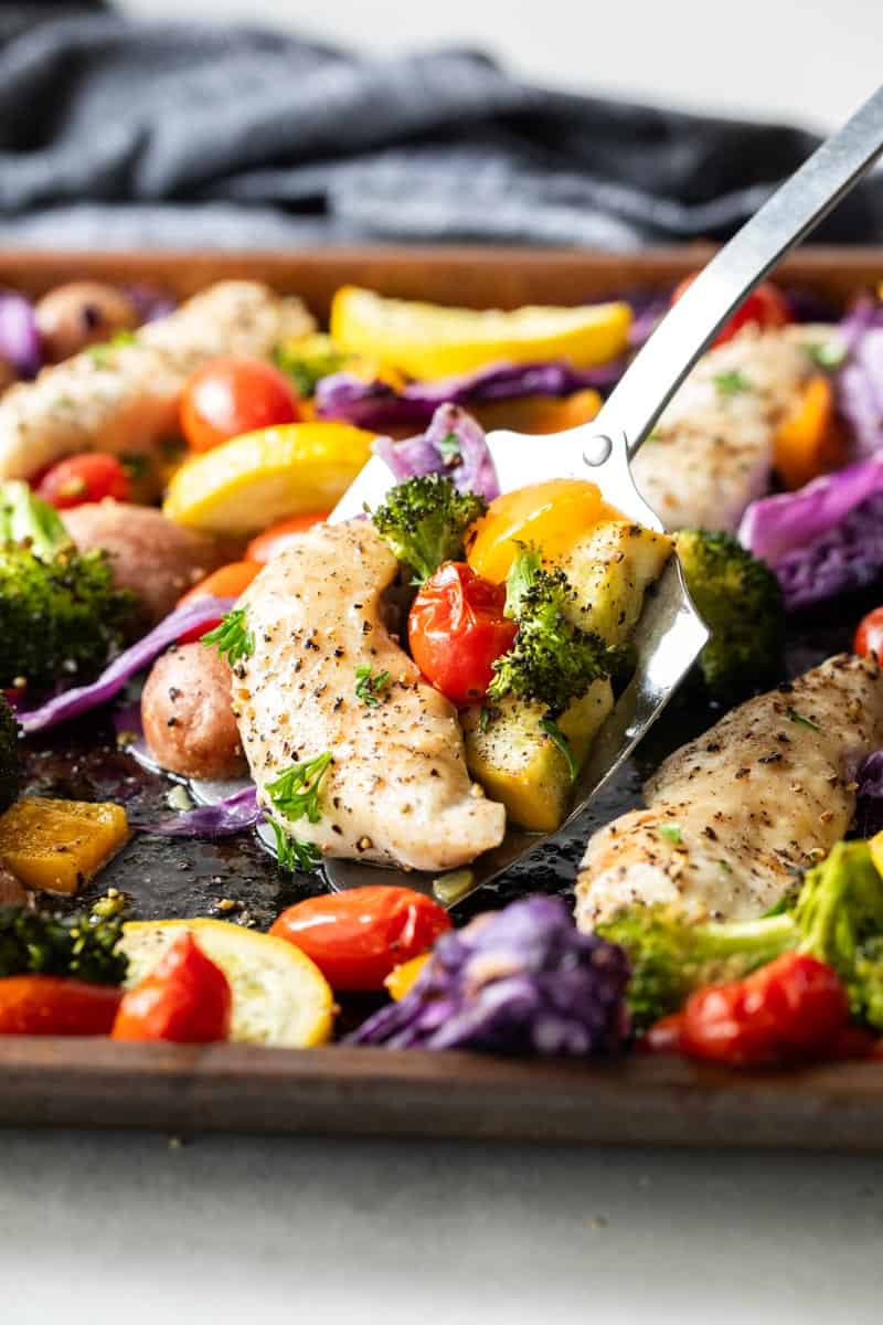 spatula scooping chicken and vegetables from sheet pan