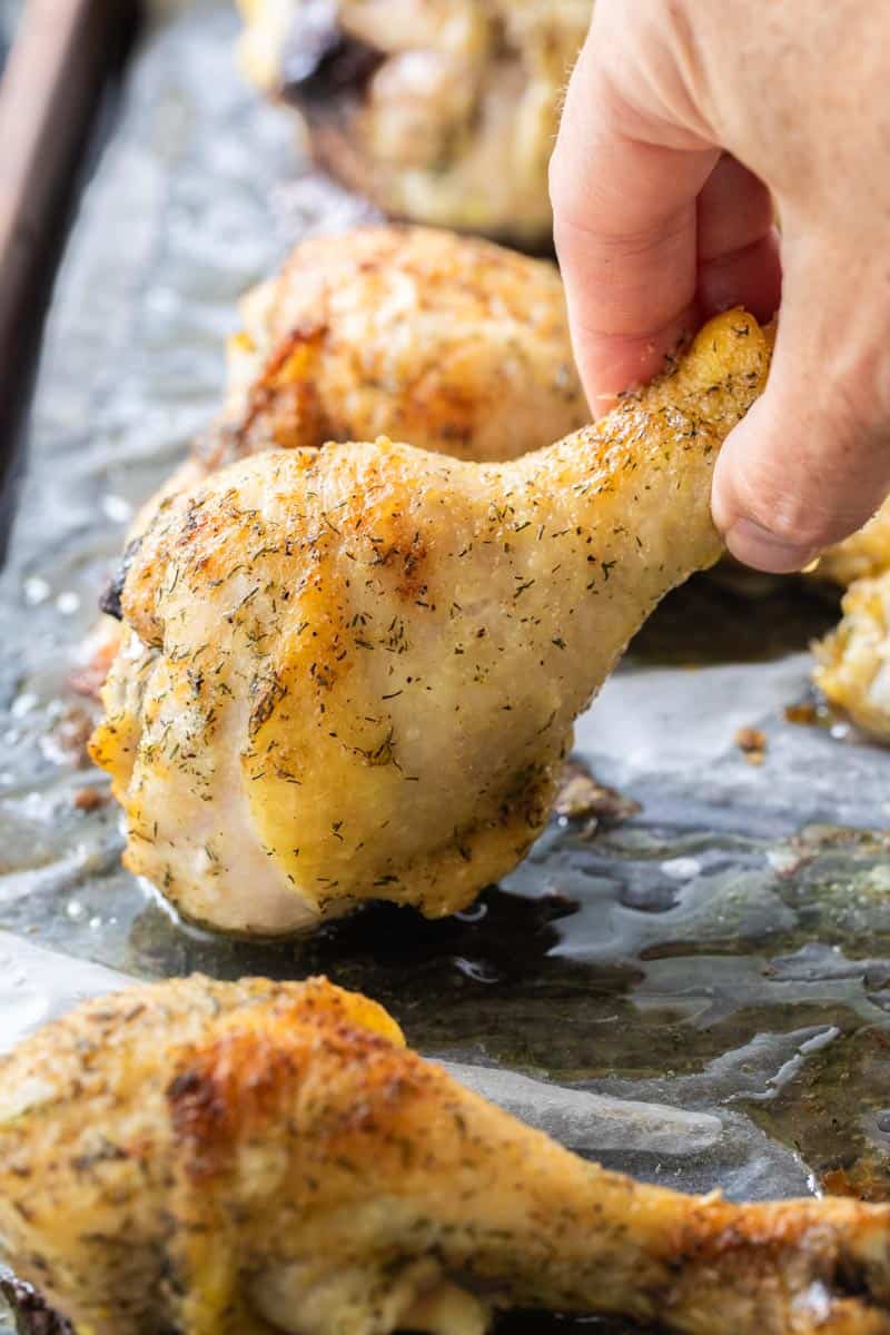 hand picking up baked chicken leg from sheet pan