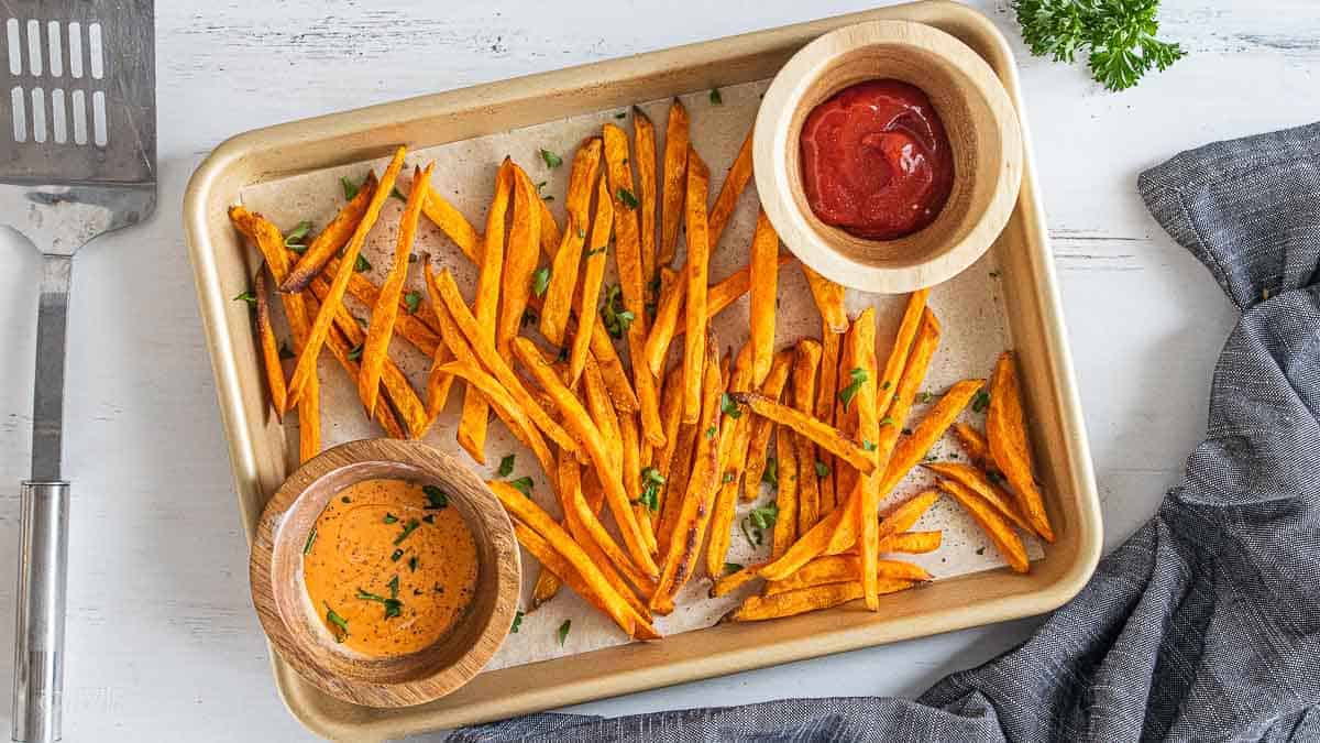 top view of sweet potato fries on parchment lined baking sheet with gluten free dipping sauces