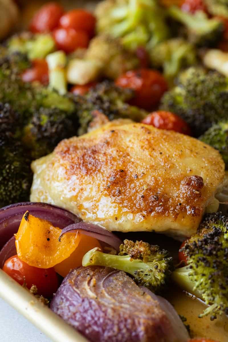 close up of a crispy chicken thigh and veggies on sheet pan