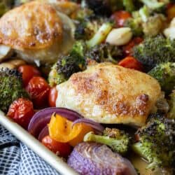 close up of baked chicken thighs on a sheet pan with roasted vegetables