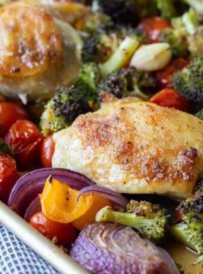 close up of baked chicken thighs on a sheet pan with roasted vegetables