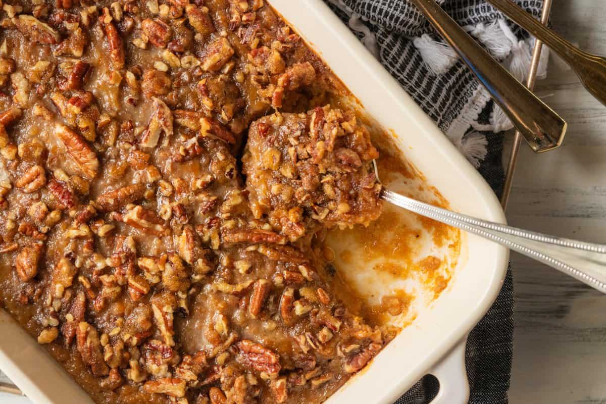 top down shot of sweet potato casserole in a white casserole pan with a spoon removing a scoop