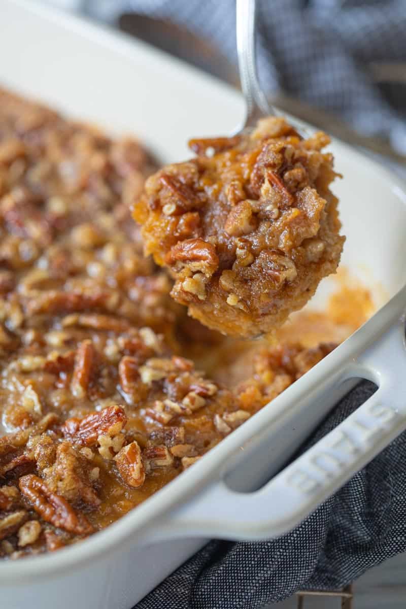 sweet potato casserole in a white casserole pan with a spoon holding up a scoop to the camera