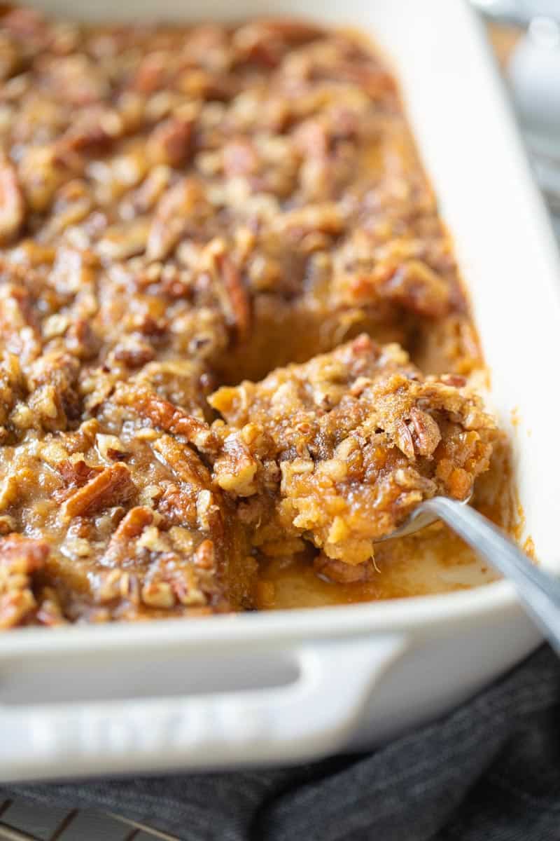 sweet potato casserole in a white casserole pan with a spoon removing a scoop