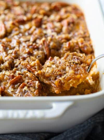 sweet potato casserole in a white casserole pan with a spoon removing a scoop