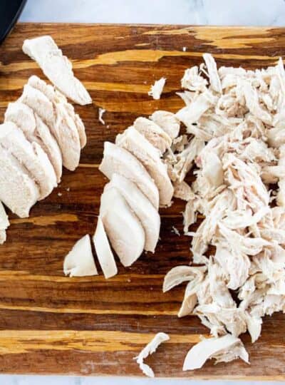 Boiled chicken breasts sliced and shredded on a cutting board