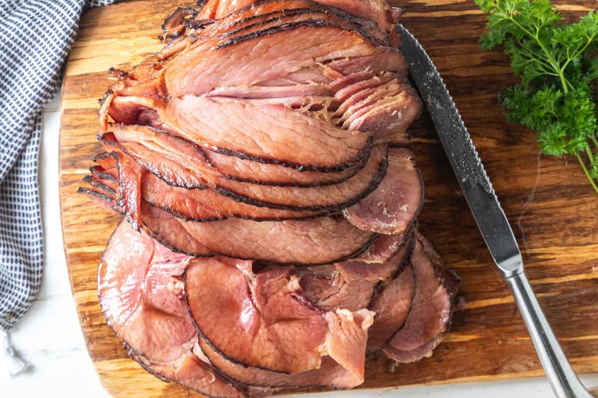 top down view of spiral ham on wooden board with carving utensils