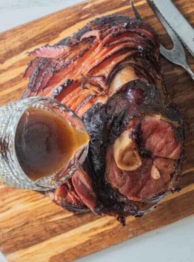 spiral ham in roasting pan being glazed with pineapple glaze