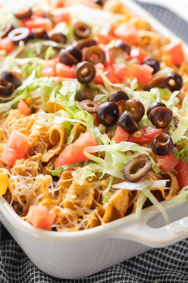 taco casserole topped with cheese, lettuce, tomato and olives