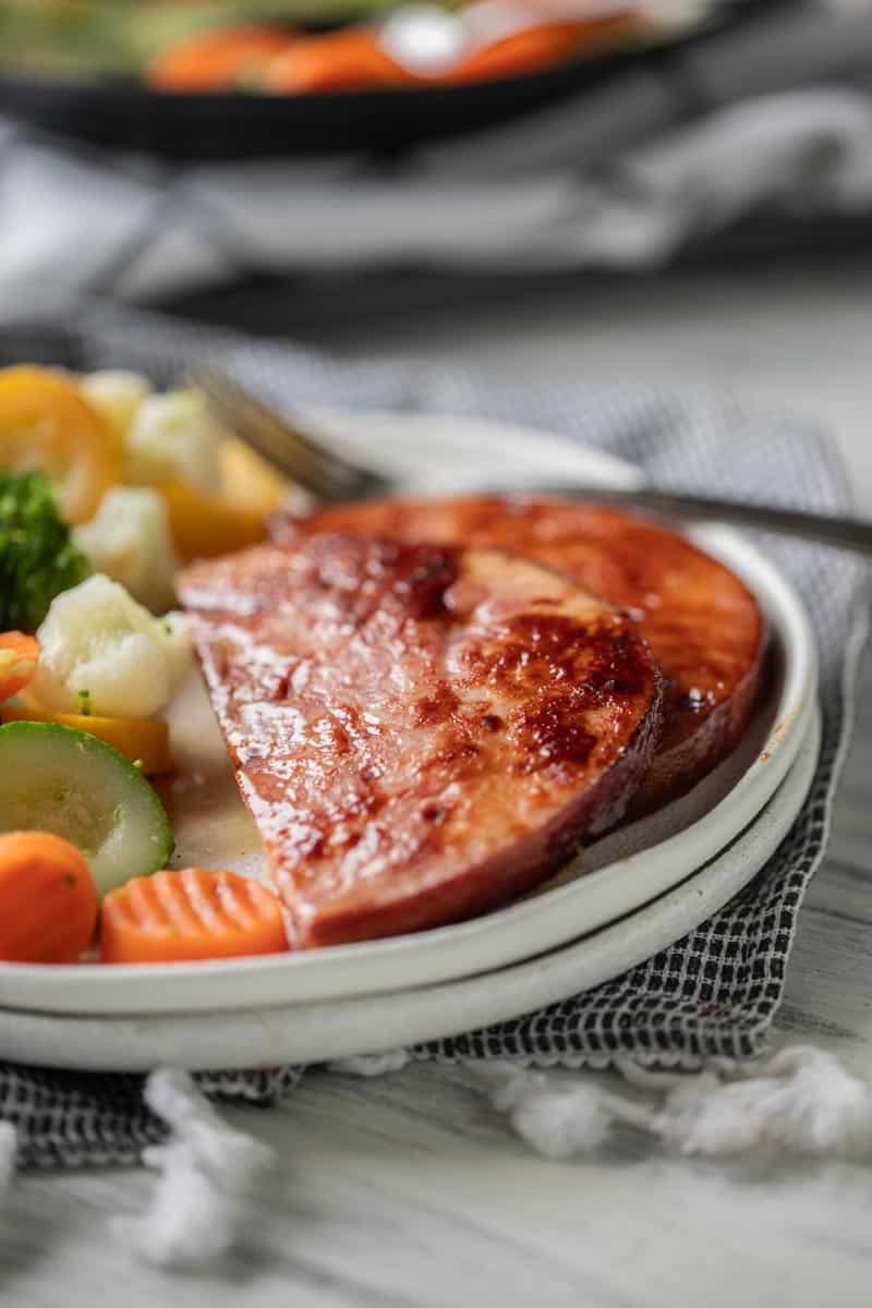 sliced ham steak on a plate with steamed vegetables