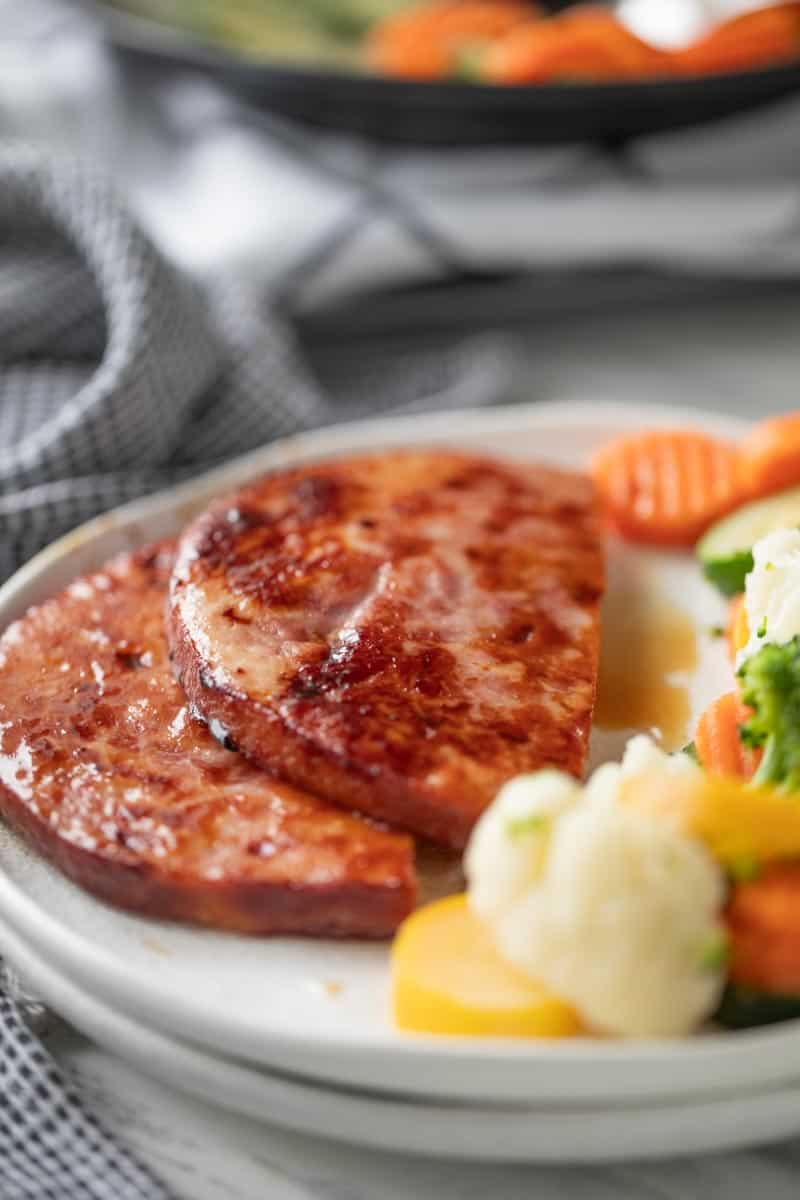 sliced ham steak on a plate with steamed vegetables