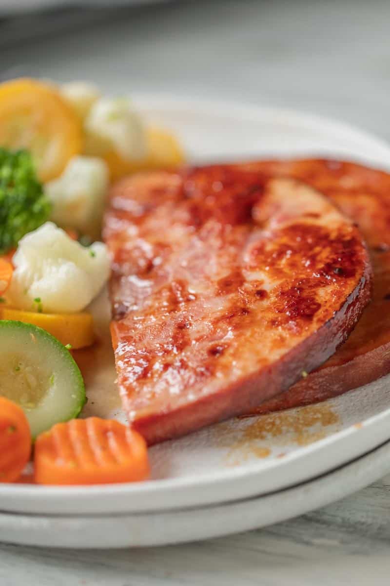 sliced ham steak on a plate with steamed vegetables