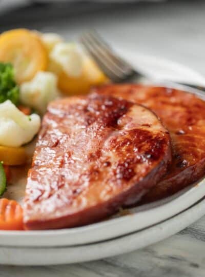 sliced ham steak on a plate with steamed vegetables