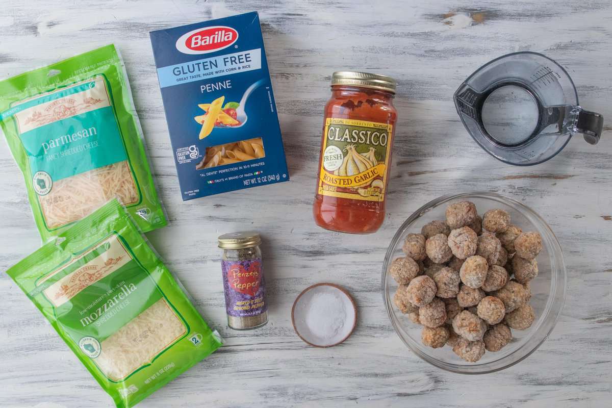 parmesan cheese, mozzarella cheese, penne, salt, pepper, pasta sauce, frozen meatballs and water on a countertop