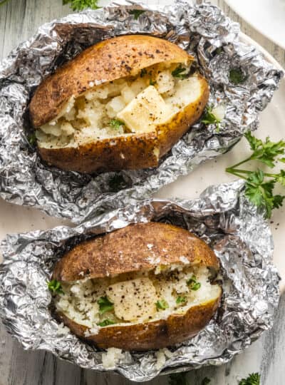 top down view of baked potatoes in foil topped with salt, pepper and butter