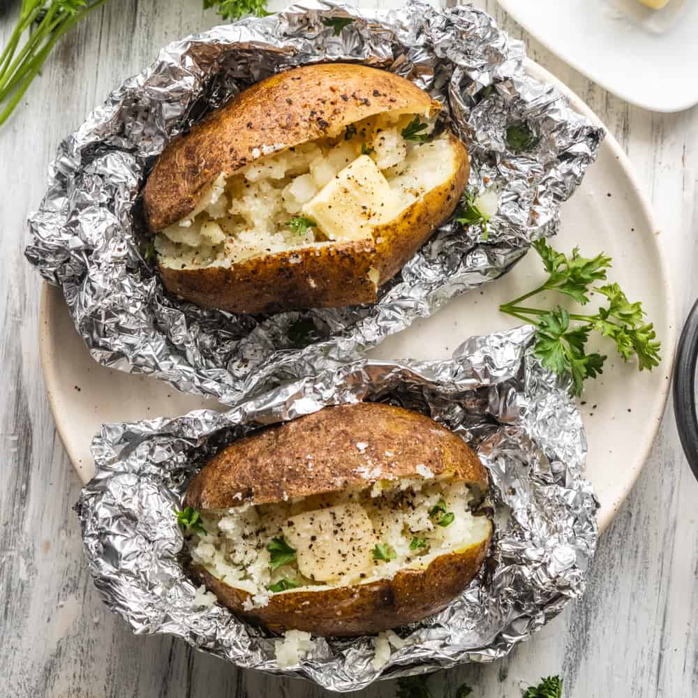 top down view of baked potatoes in foil topped with salt, pepper and butter