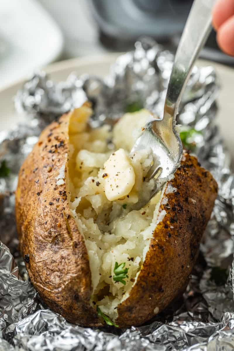 fork scooping into an oven baked potato topped with spices and butter