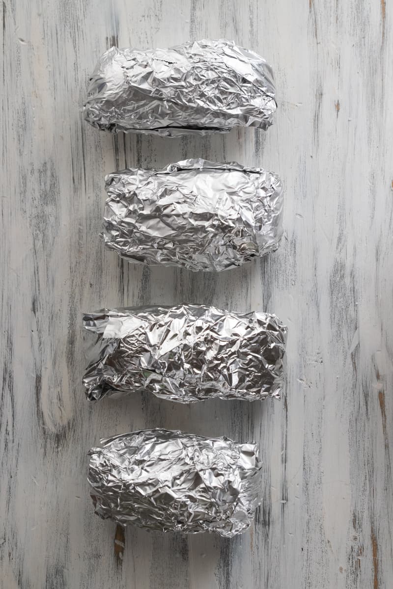 four potatoes wrapped in aluminum foil