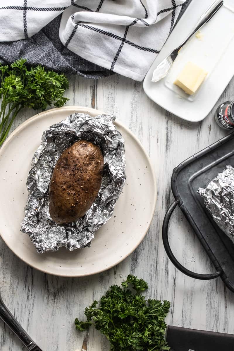 baked potato in foil on a plate next to butter