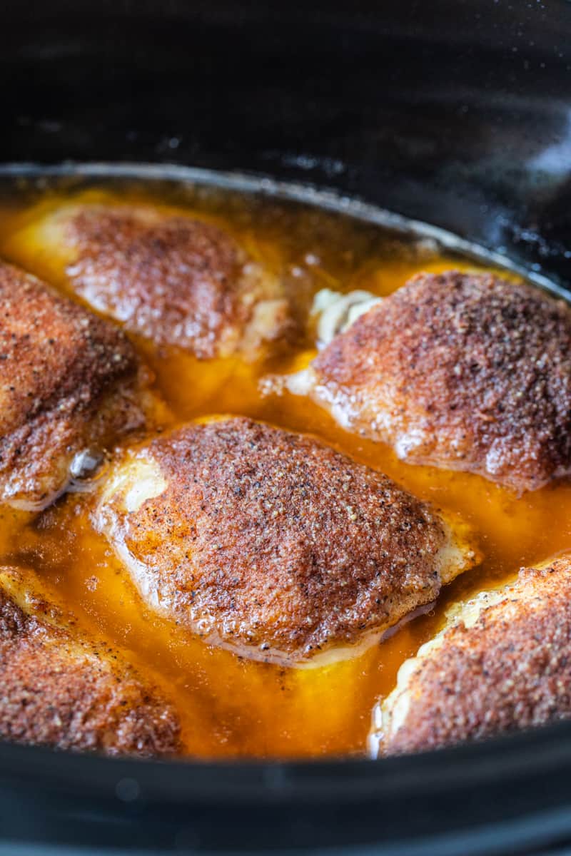 close up of cooked and seasoned chicken thighs in a slow cooker