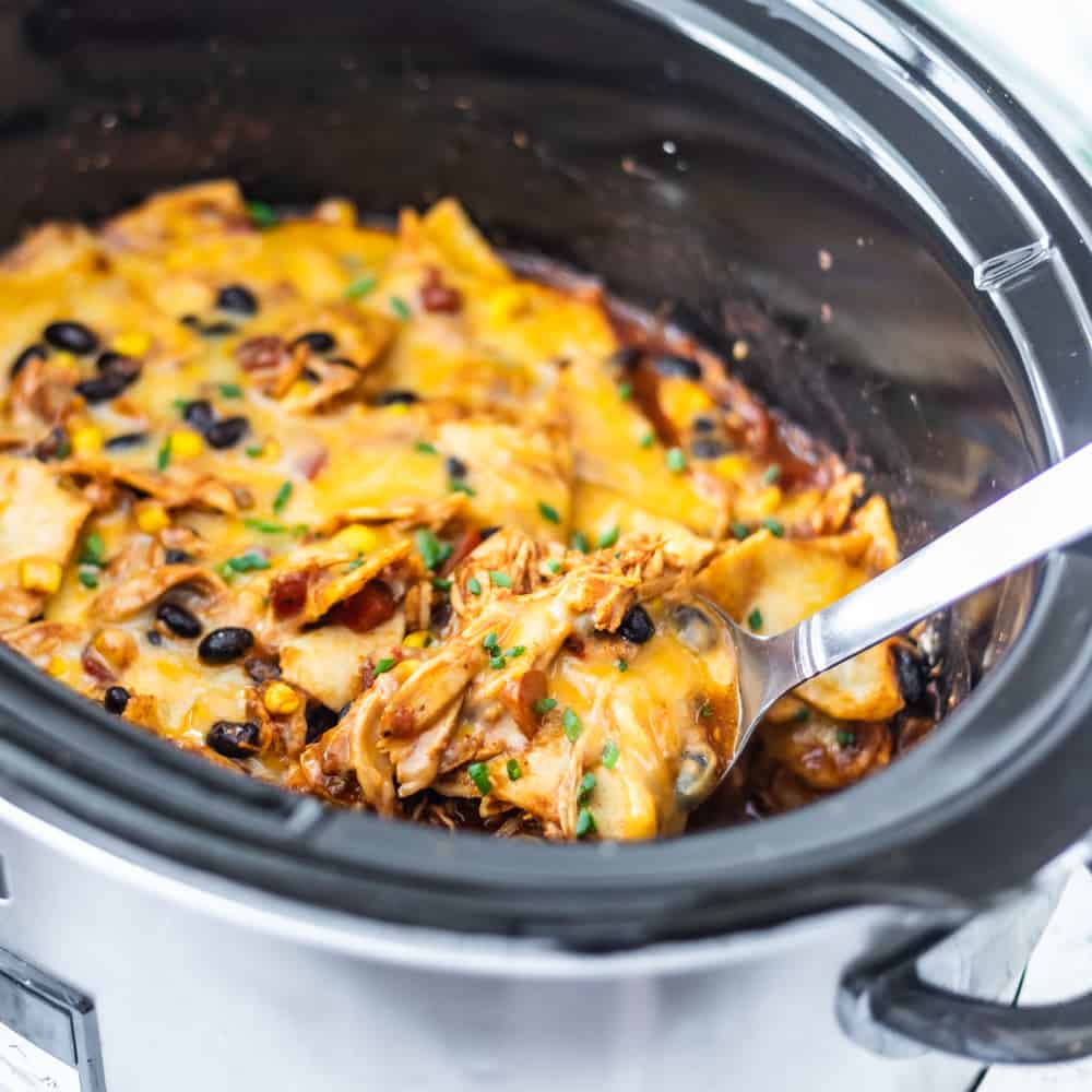 chicken enchilada casserole in a crockpot with a spoon removing some