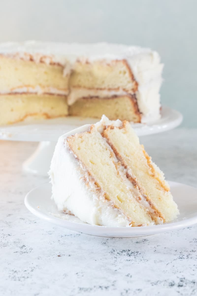 slice of gluten and dairy free cake on a plate with the rest of the cake in the background