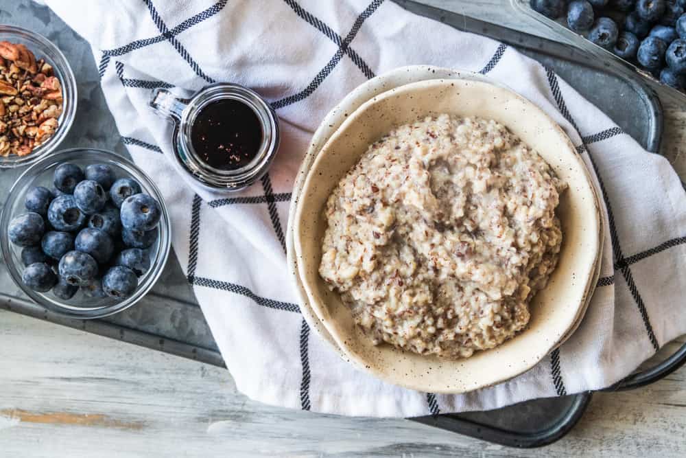 bowl of pecans, bowl of blueberries, bowl of syrup and bowl of oatmeal with flaxseed on countertop