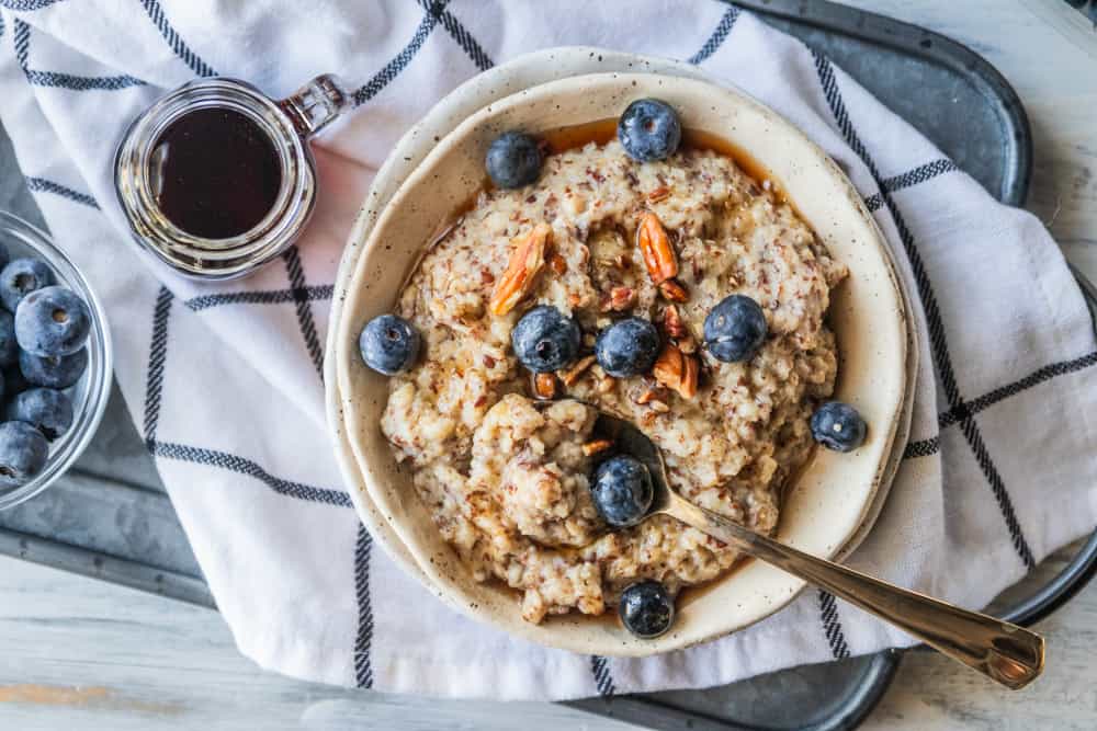 top down view of a bowl of oatmeal topped with syrup, nuts and blueberries next to a small bowl of blueberries and a bowl of syrup