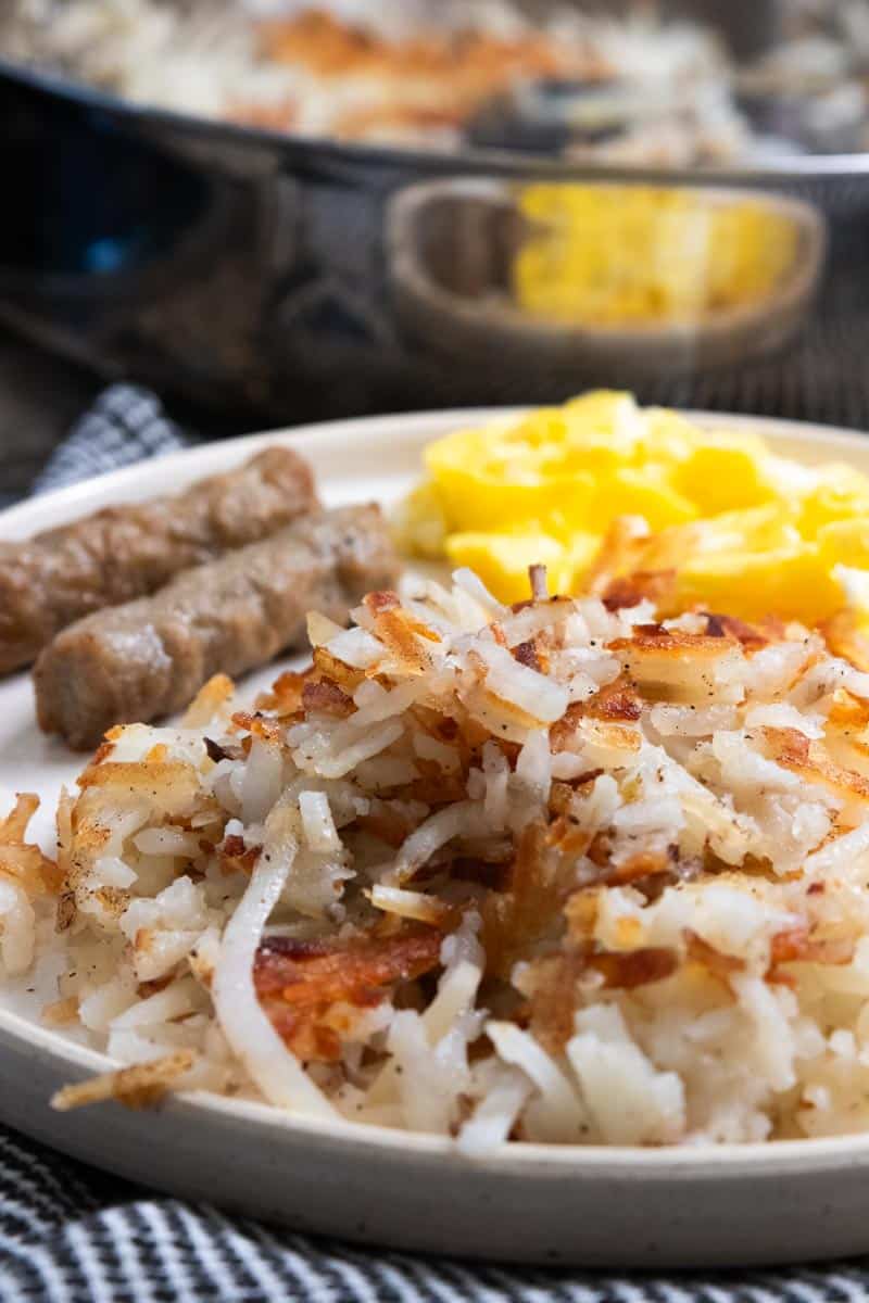 up close pic of hashbrowns on a plate with eggs and sausage